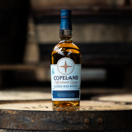 A bottle of Merchants' Quay blended Irish whiskey by Copeland Distillery, with a still from the distillery in the background.