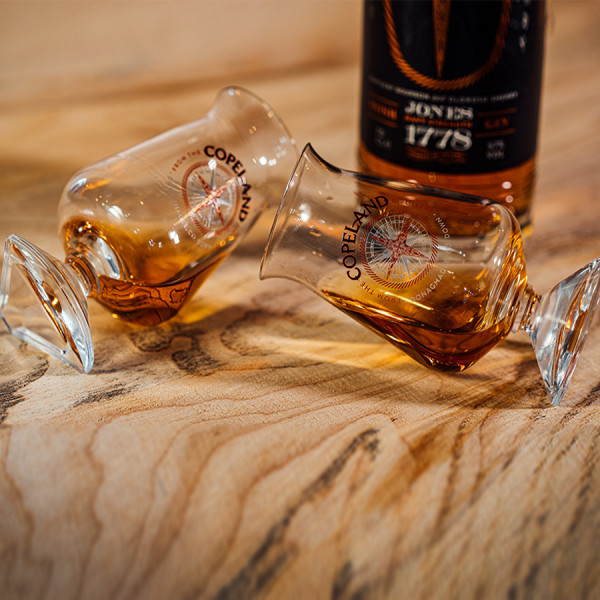 Two Túath whiskey glasses sat on their side in front of a bottle of Jones 1778 Navy Strength Gin by Copeland Distillery.